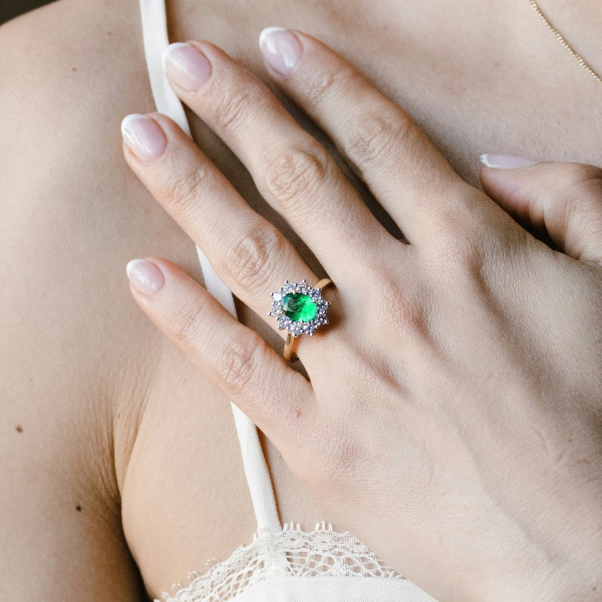 Gold emerald and diamond cluster ring with an oval emerald, worn on the finger.