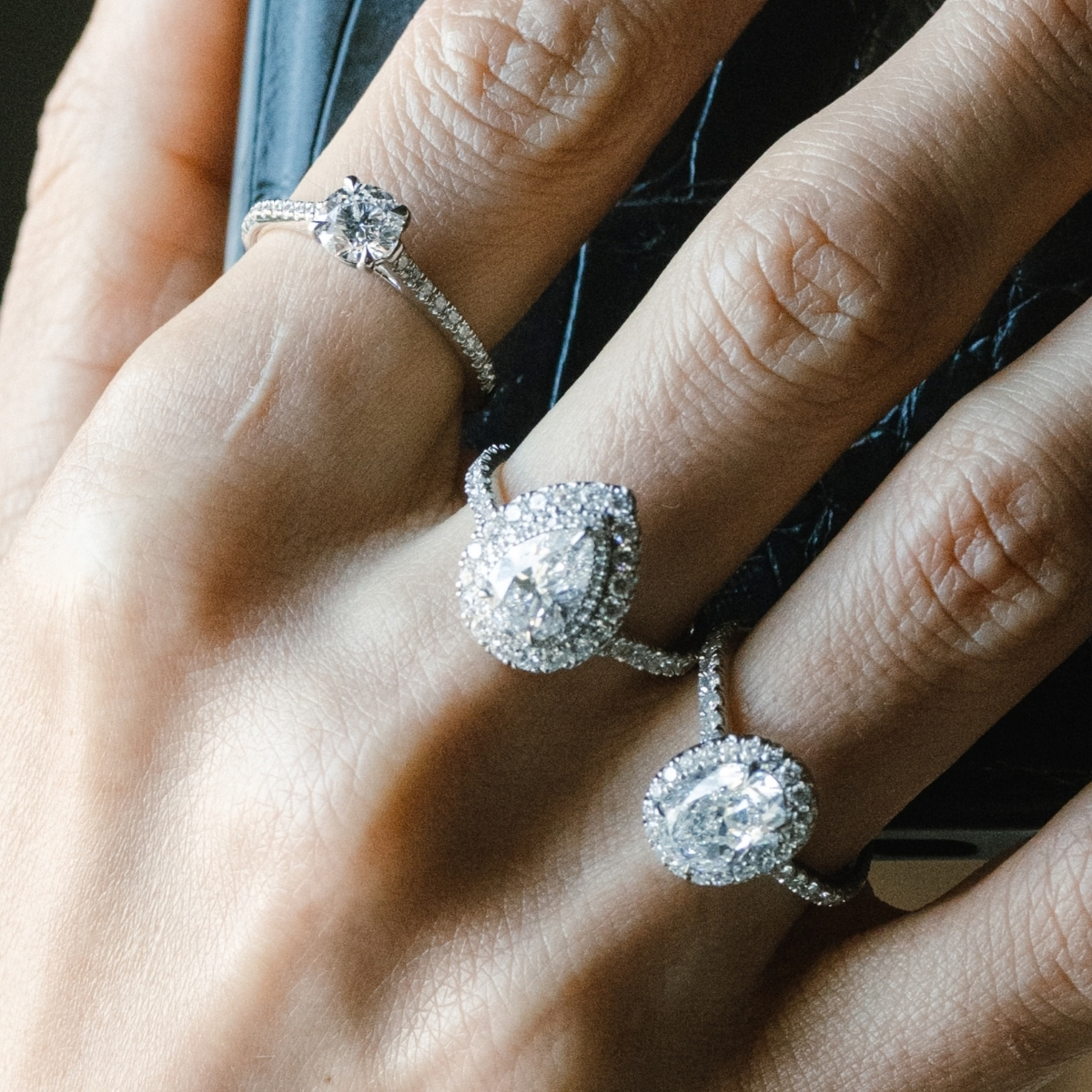 Halo set pear cut diamond engagement ring, worn stacked with an oval halo ring and a solitaire.