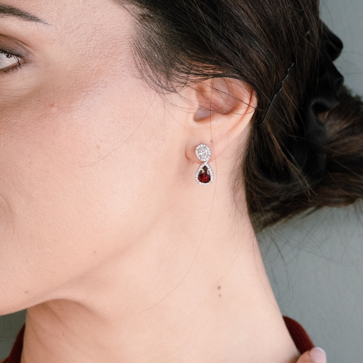 Halo set pear ruby and diamond drop earrings, worn with hair swept back.
