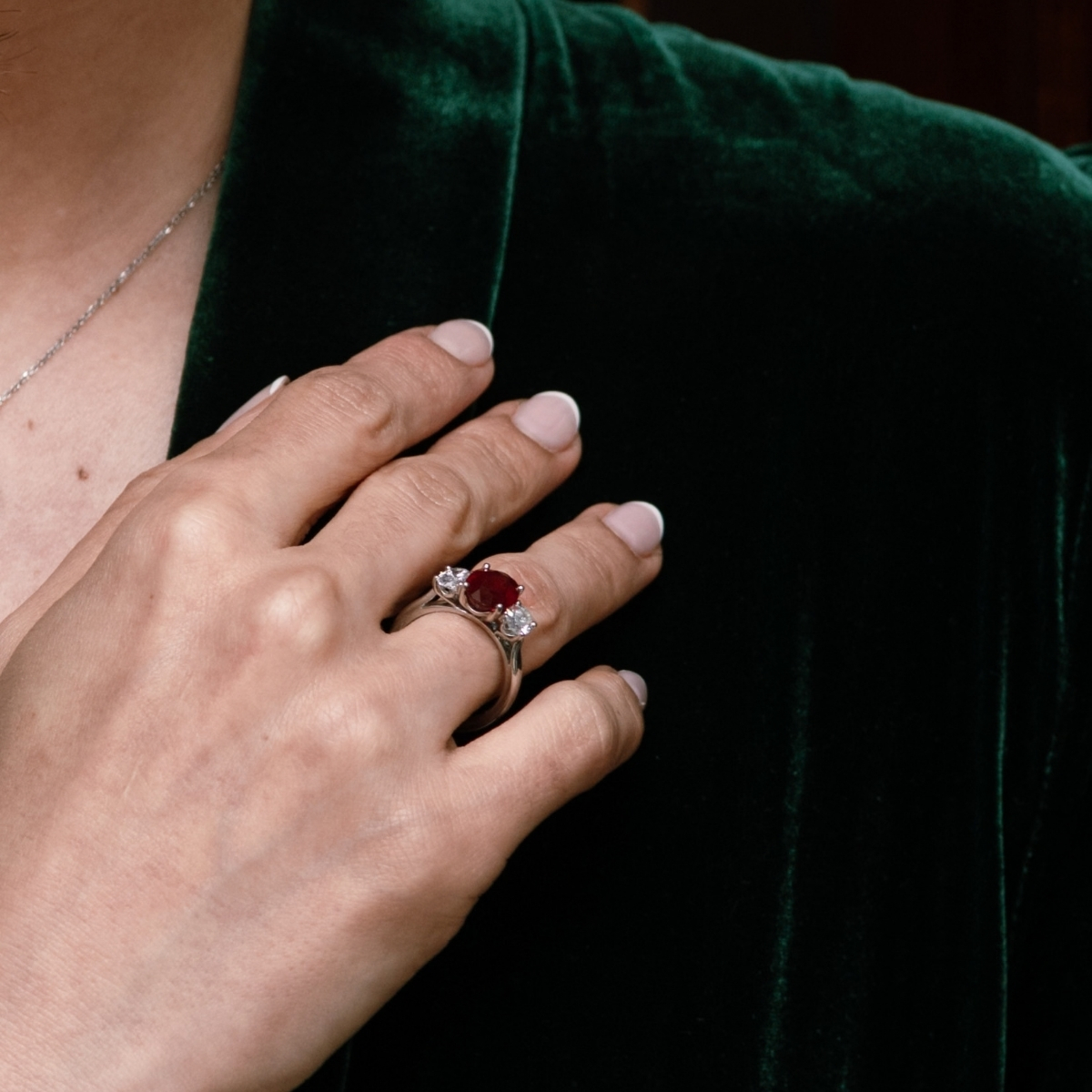 Platinum oval ruby and diamond three-stone ring, worn on the hand against green velvet.
