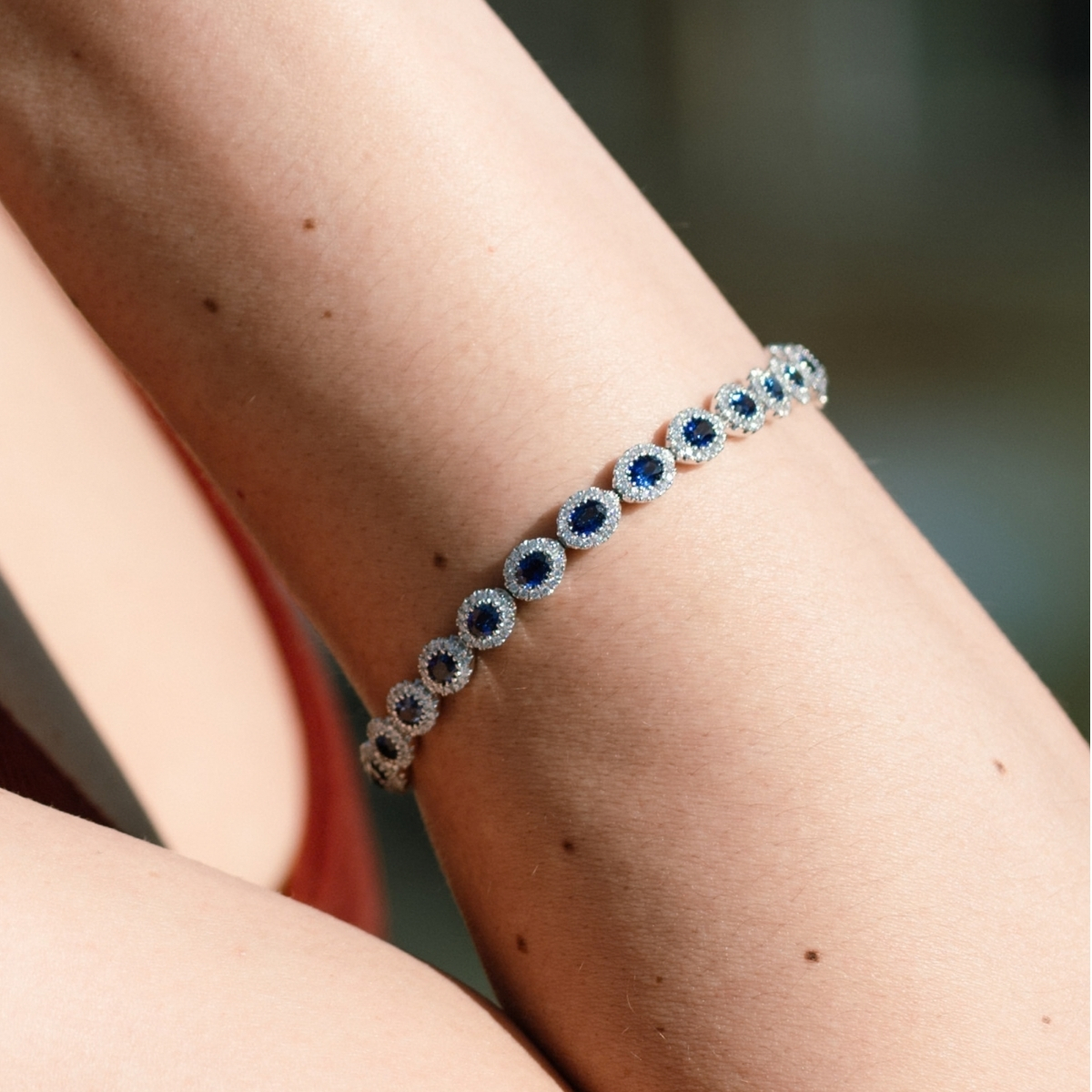 Sapphire and diamond halo set bracelet in white gold, worn on the wrist.