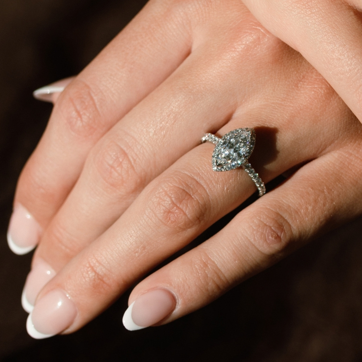 Marquise cut diamond halo engagement ring in platinum, worn on the finger with diamond-set shoulders.