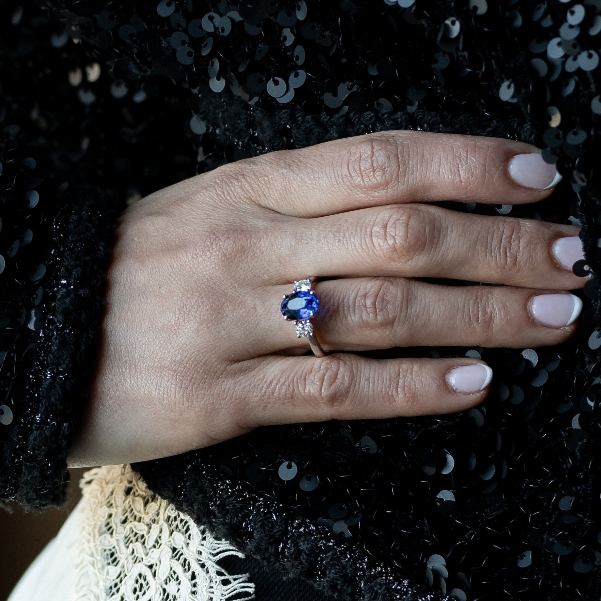 Platinum oval sapphire and diamond engagement ring, worn on the hand against black sequins.
