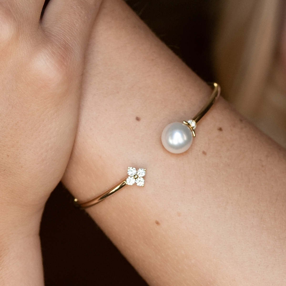 Yellow gold pearl and diamond open bangle with a diamond flower end, worn on the wrist.