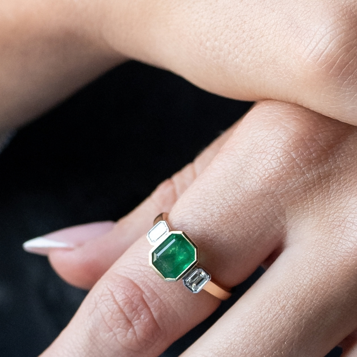 Emerald three-stone ring rubbed over in gold with baguette diamonds, worn on the finger.