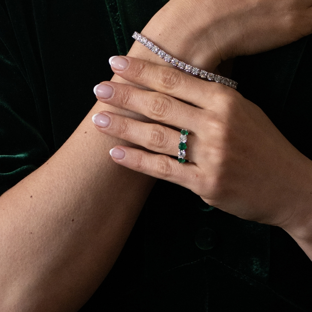 Platinum emerald and diamond five-stone ring, worn on the finger with a diamond line bracelet.