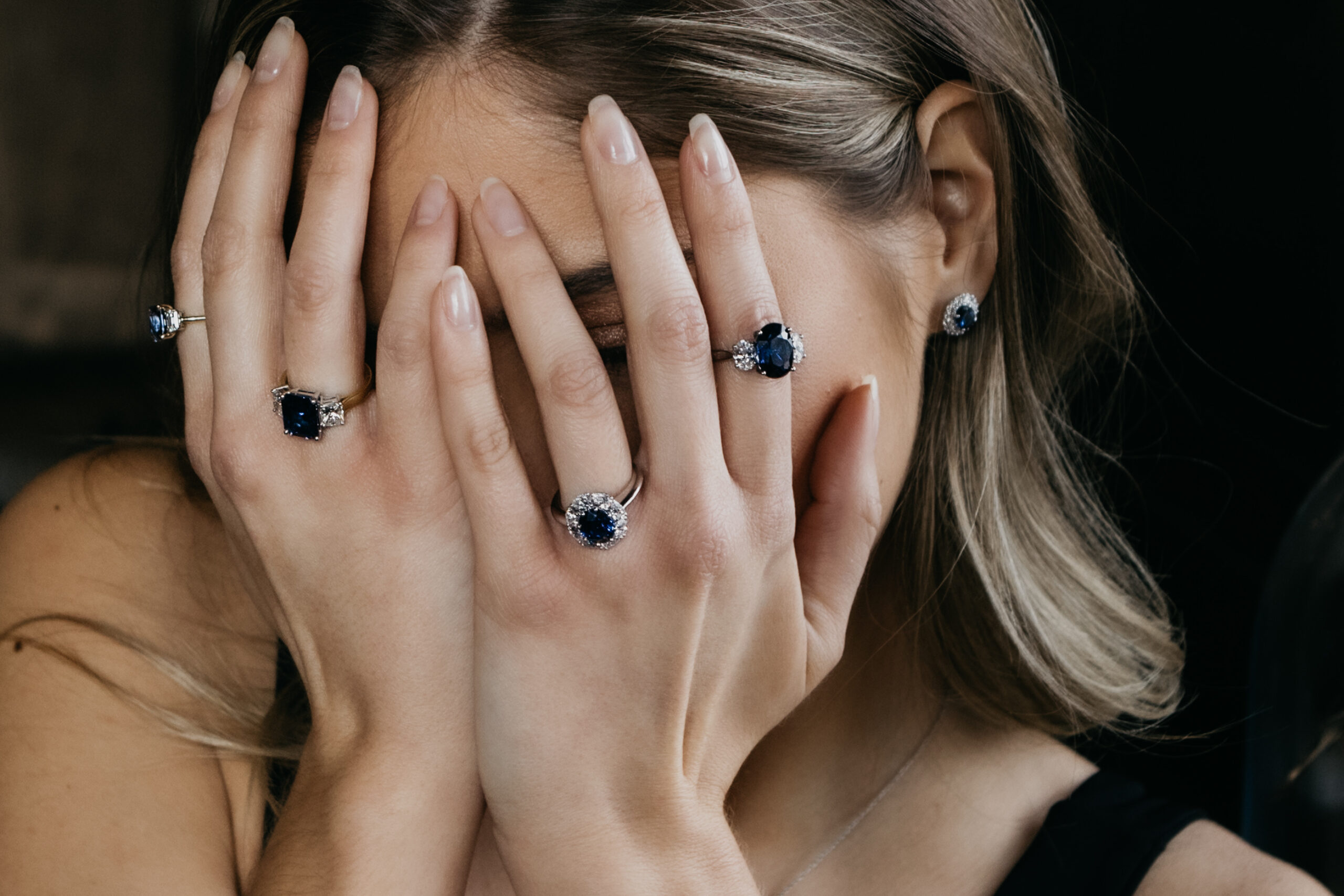 A woman wearing solitaire rings and three-stone rings, which are sapphire