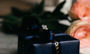 A diamond jewellery ring sitting on top of a black fine jewellery box with two roses behind it. Product photography image.