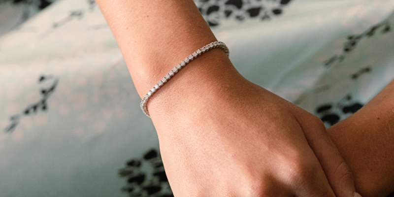 Woman's hand placed over her other hand with a tennis bracelet on in summer weather.