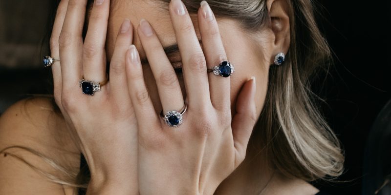 A woman wearing solitaire rings and three-stone rings, which are sapphire