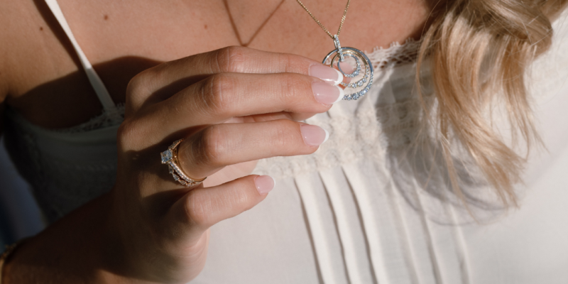 Woman holiday a diamond pendant with a diamond ring on her finger in the sunshine. close up